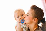 Young mother kissing baby with soother
