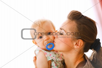 Young mother kissing baby with soother
