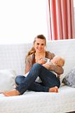 Young mother sitting on sofa and feeding her baby 
