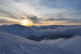 Setting sun in cloudy winter mountains