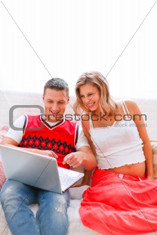 Happy young man showing his pregnant wife something in laptop
