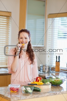 Woman nibbling bell pepper while preparing healthy salad