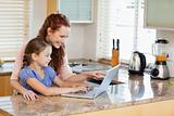 Mother and daughter with laptop behind the kitchen counter