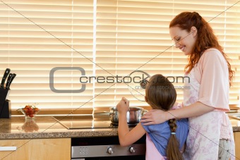 Cheerful mother showing her daughter how to cook
