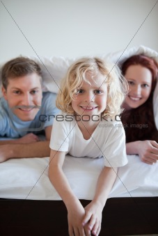 Cheerful boy under the bed cover with his parents