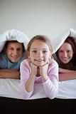 Smiling girl under bed cover with her parents