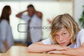 Sad looking boy with arguing parents behind him