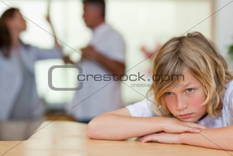 Worried looking boy with fighting parents behind him