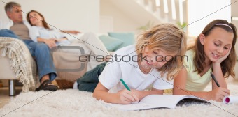 Siblings doing their homework on the carpet with parents behind them