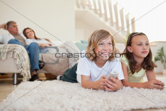 Siblings lying on the carpet watching tv