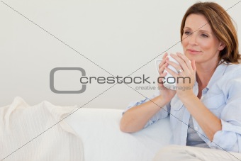 Thoughtful woman with cup of coffee on sofa
