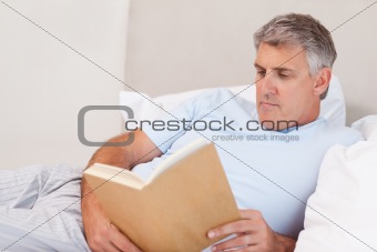Mature man reading book in bed