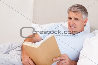 Smiling man with book in bed