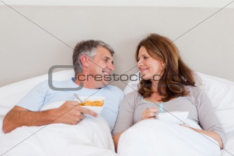 Happy couple eating cereals in bed
