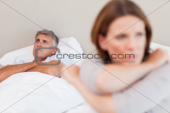 Sad man in bed with his wife in the foreground