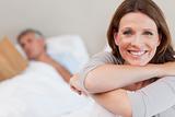 Smiling woman on bed with reading husband in the background
