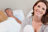 Smiling mature woman on bed with reading husband behind her