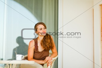 Thoughtful young female  sitting on terrace with cup of tea and looking in corner
