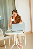 Smiling pretty woman having cup of tea and looking in laptop
