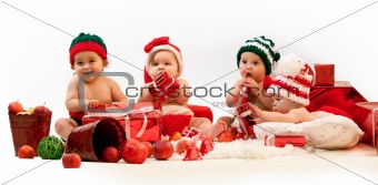 Four babies in xmas costumes playing among gifts