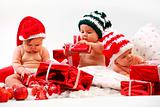 Three babies in xmas costumes playing with gifts