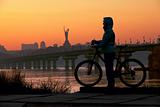 Young woman with bicycle against sky at sunset