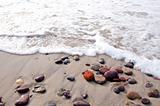 Sea waves beat stones lying in sand on coast line.