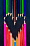 Colorful pencils on dark background in a shape of a heart