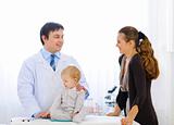 Pediatric doctor talking with mother while baby playing with stethoscope 

