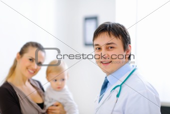 Portrait of pediatric doctor and smiling mother with lovely baby in background
