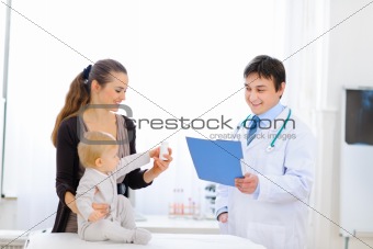 Mother and baby holding bottle of vitamins on examination of pediatric doctor
