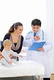 Pediatric doctor talking with mother while baby sitting on table
