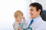 Portrait of happy cute baby with stethoscope on hands of pediatrician
