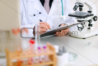 Medical doctor writing something in clipboard at office table. Close-up.

