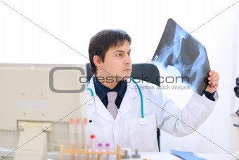 Medical doctor sitting at office table and analyzing patients roentgen
