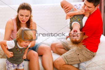 Parents having fun with twins daughters on couch
