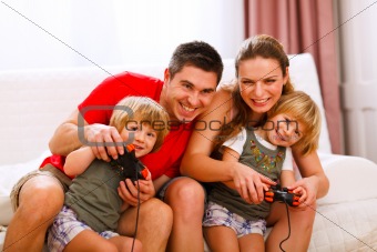 Mom and dad playing with twins daughter on console
