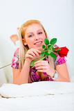 Smiling young woman laying on white couch with red roses in hand
