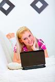 Smiling young woman laying on white couch with laptop
