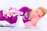Flowers in vase on table and woman laying on sofa in background
