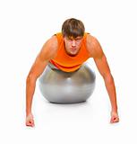 Young man in sportswear making push up exercise on fitness ball isolated on white
