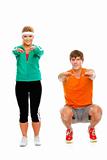 Portrait of healthy girl and man in sportswear sitting on squat isolated on white
