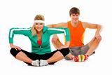 Fitness young woman and man in sportswear doing stretching exercise on floor
