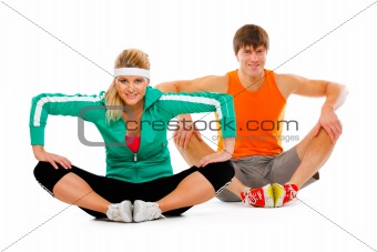 Fitness young woman and man in sportswear doing stretching exercise on floor
