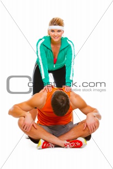 Fitness girl in sportswear helping guy doing stretching exercise on floor
