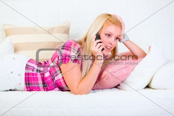Interested girl laying on white divan and speaking phone
