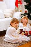 One of twins girl sitting with present with serious expression 
