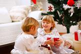 Two twins girl sitting with presents near Christmas tree
