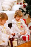 Two happy twins girl opening presents near Christmas tree

