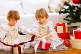 Two happy twins girl opening presents near Christmas tree
